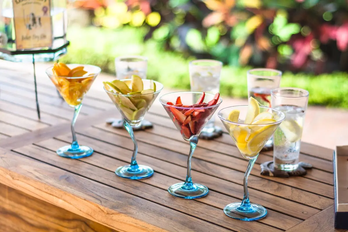 Vibrant fruit-filled cocktail glasses displayed on a wooden table outdoors, perfect for a summer gathering.