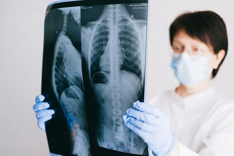 A medical professional analyzes a chest x-ray wearing gloves and a mask in a clinical setting.