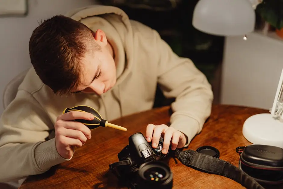 Young photographer diligently cleaning DSLR camera parts at a wooden table under warm light.