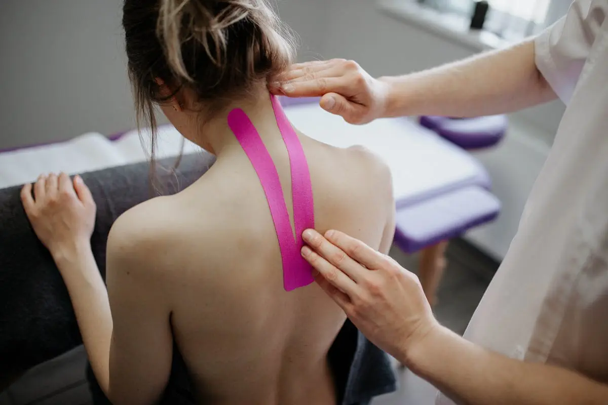 A healthcare professional applies kinesiology tape on a woman’s neck for therapeutic treatment.