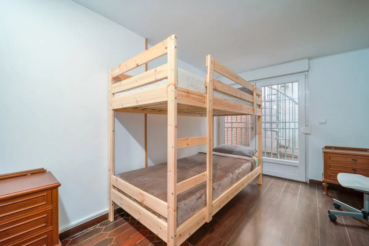 Neat bedroom with a wooden bunk bed and minimalist decor, featuring natural lighting.