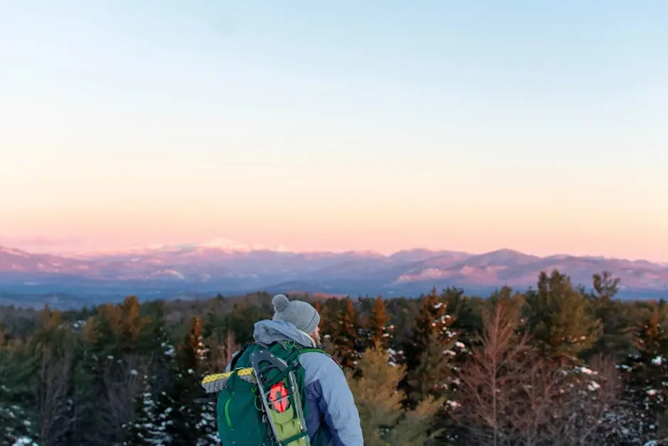 A backpacker overlooks snow-covered mountains during a vibrant winter sunset in Lincoln, New Hampshire.