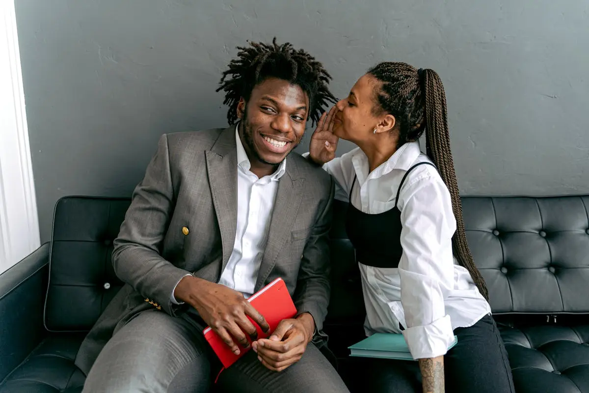 Two professionals sharing a secret on a modern black couch, indoors.