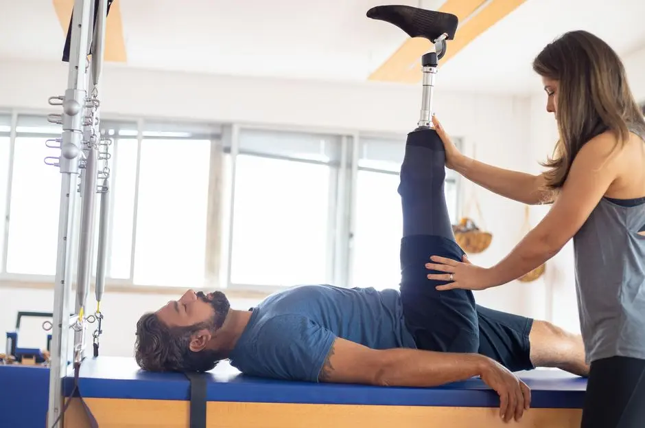 Personal trainer assists amputee in rehabilitation exercise indoors.