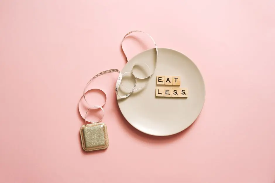 A motivational image featuring a plate with scrabble tiles spelling ‘Eat Less’ on a pink background.