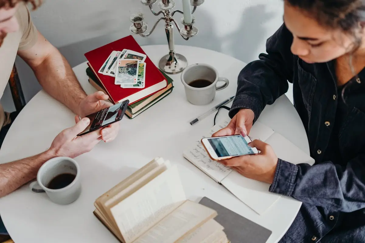 A couple texting with coffee and books at a home table, sharing a cozy morning moment.