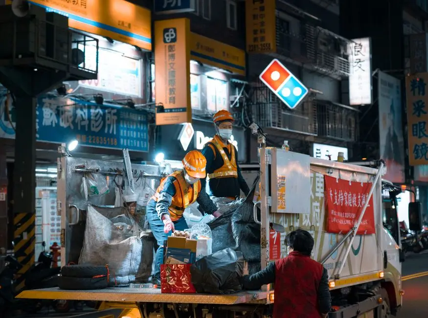 Garbage collectors in safety gear working at night in a vibrant city environment.