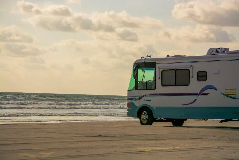 An RV parked on a sandy beach with the ocean and cloudy sky in the background.