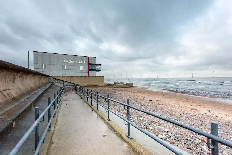 A modern theatre near a windy beach with wind turbines on the horizon in England.