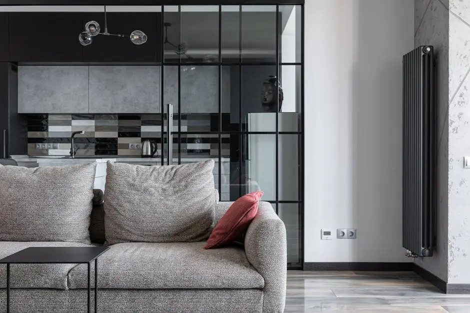 Contemporary living space featuring a stylish gray sofa, red cushion, and a view into a modern kitchen.