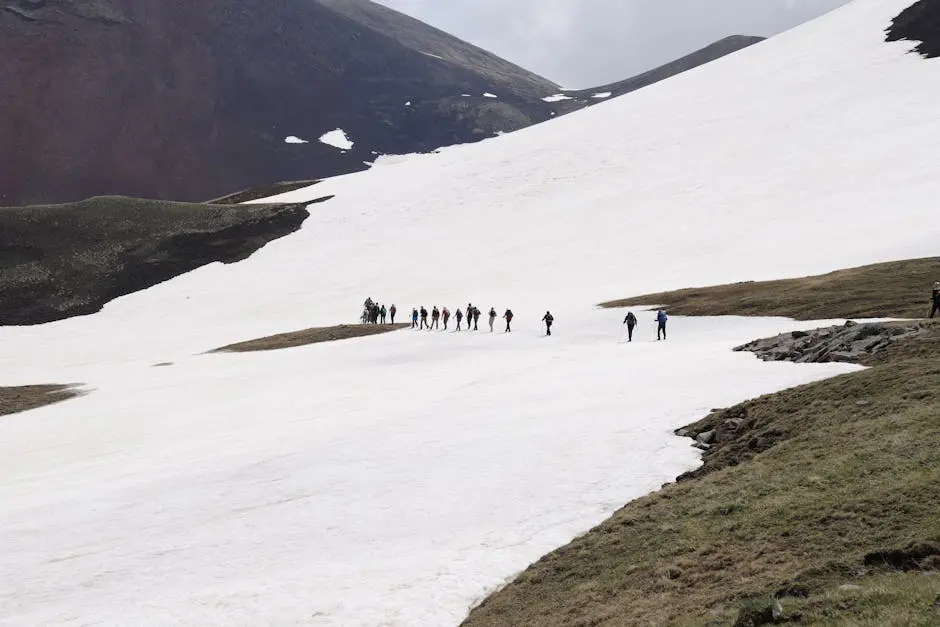A group of hikers crossing a snow-covered mountain with dramatic scenery in the background.