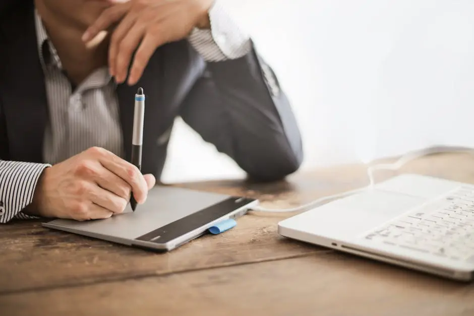 A professional working with a graphic tablet and laptop in a modern office environment.