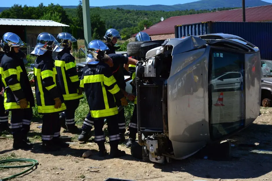Firefighters attending to an overturned vehicle at an accident scene. Daylight outdoor operation.