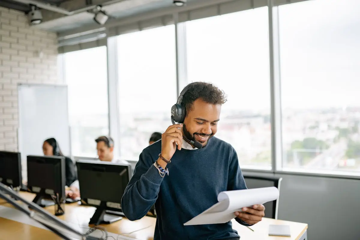 Friendly call center agent engaged in small business conversation while reviewing documents at his desk.