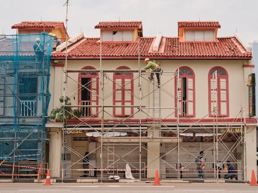 Workers on scaffolding renovating a historic building facade with red roof and tall windows.