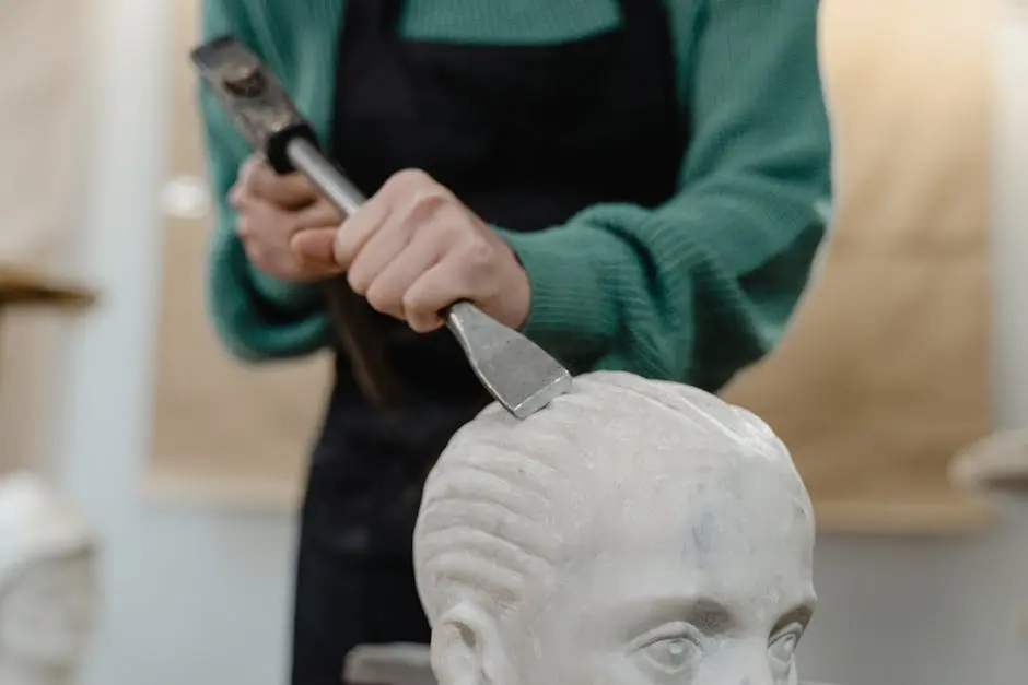 Artisan sculpting marble using chisel and hammer, focusing on head detail.