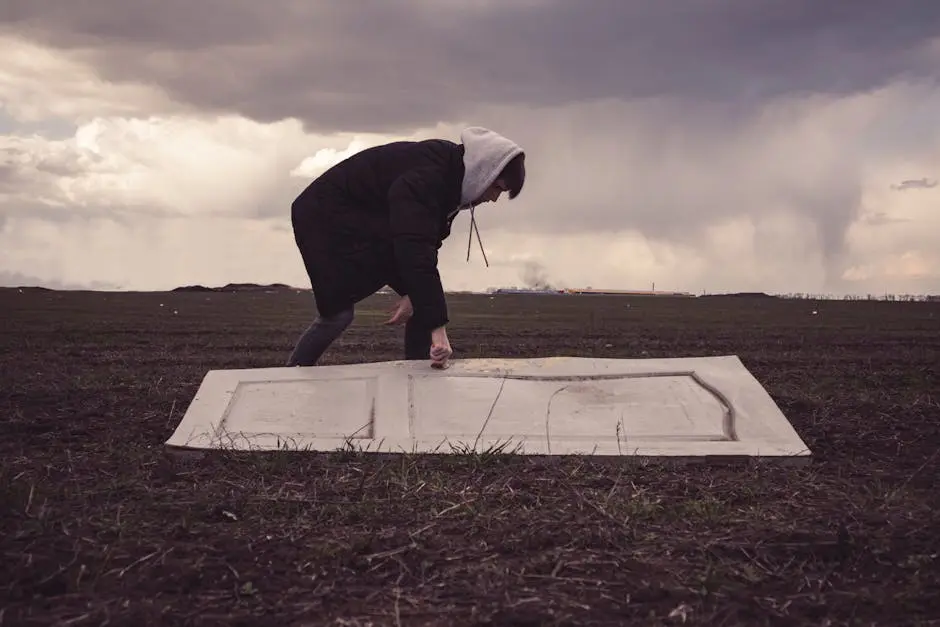 Person in hoodie placing door on grass under stormy sky in Ukraine.