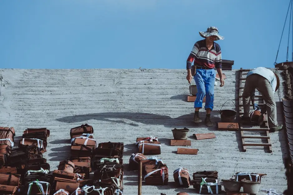 Two construction workers installing roof tiles on a building under a clear blue sky.