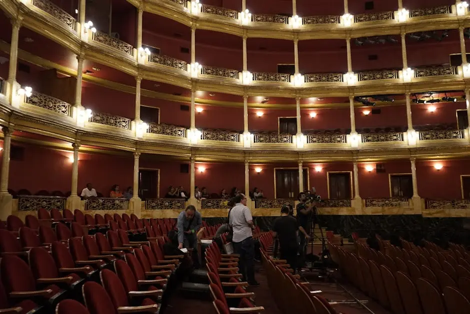 View of a classic theater interior with red seats and a camera crew setting up, capturing the venue&rsquo;s grandeur.