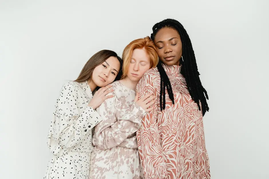 Three diverse women in stylish dresses embrace, showcasing modern fashion and friendship.
