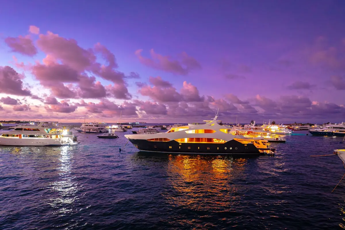 A scenic view of luxury yachts illuminated at sunset in the Maldives, offering a serene travel experience.