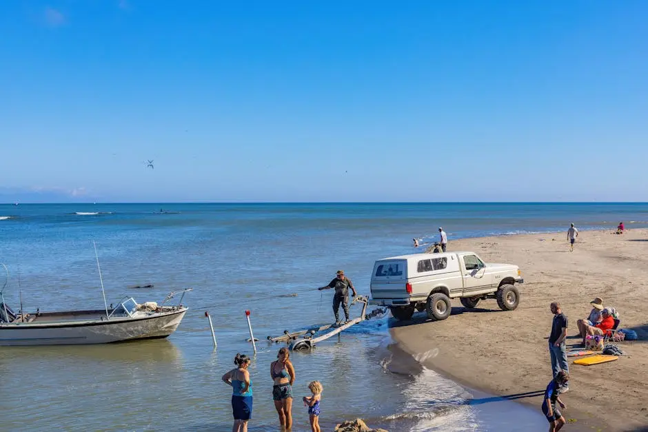 A family enjoys a sunny day at the beach while a truck assists with a boat trailer.