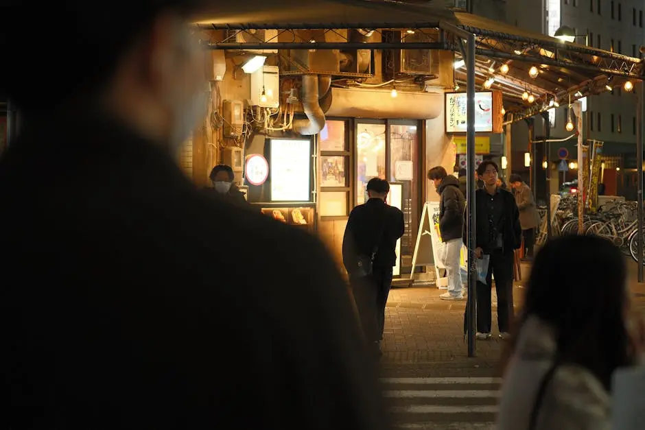 Urban scene at night with people outside a lit street restaurant.
