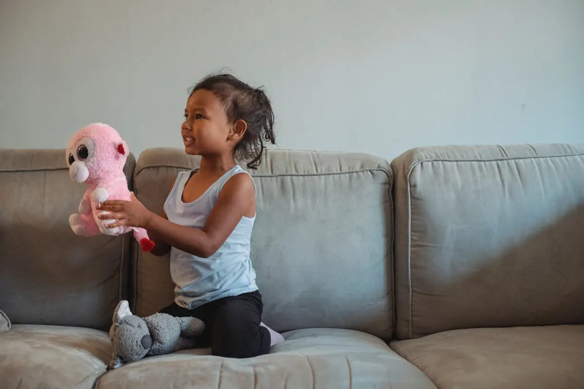 A cheerful child playing with a stuffed animal on a comfy sofa indoors.