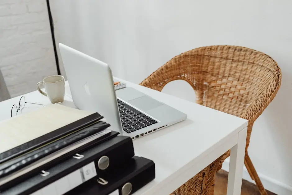 A cozy home office setup featuring a laptop, binders, and wicker chair for productive remote work.