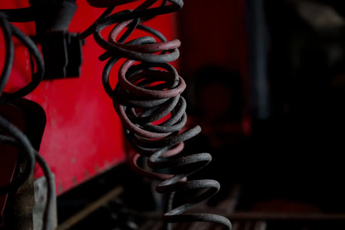 Detailed view of aged coiled springs with a red industrial backdrop, showcasing metal textures.