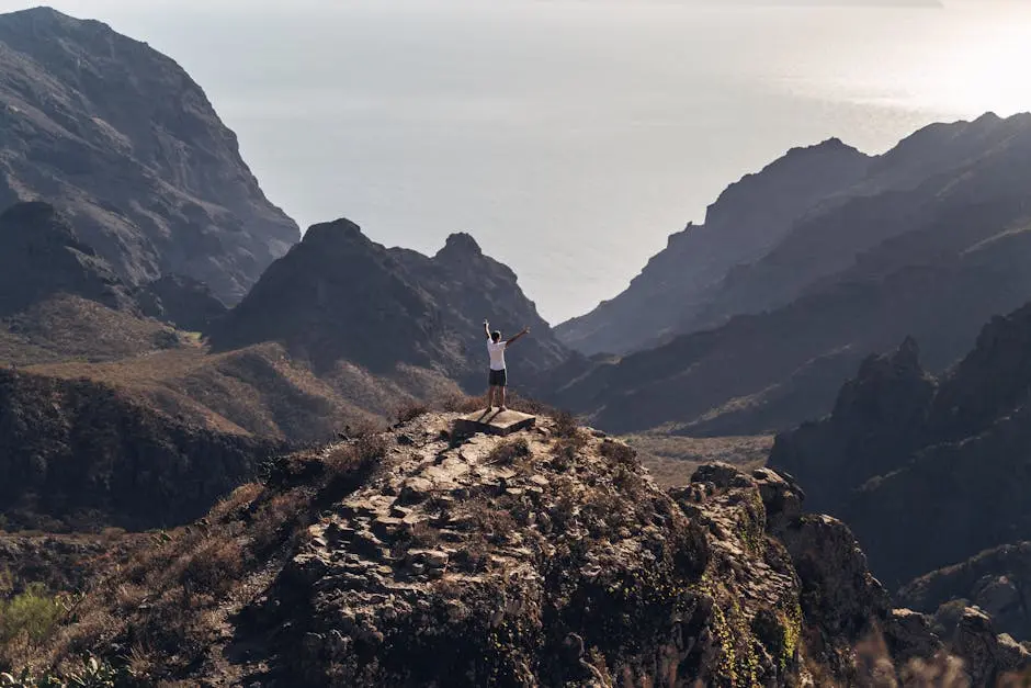 A person stands triumphantly on a mountain peak in Tenerife, admiring the expansive landscape.