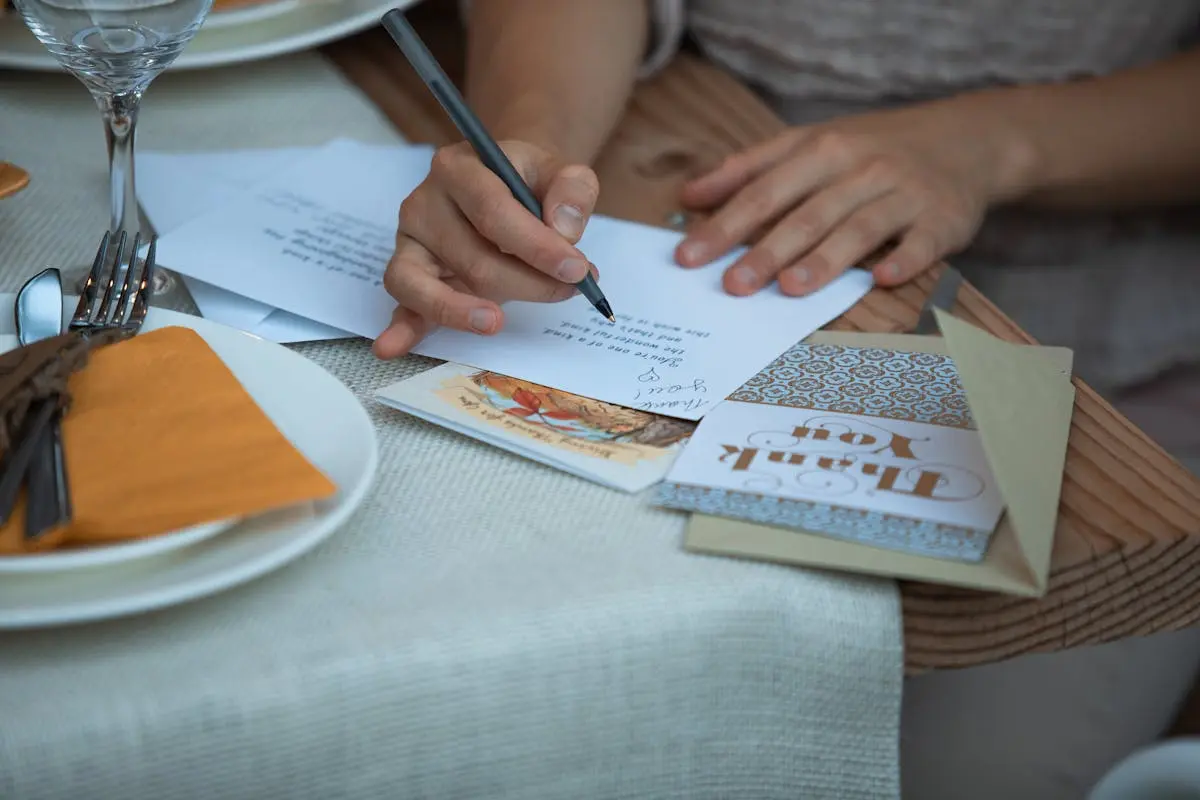 A person writing a Thanksgiving thank you note at a dinner table, surrounded by festive decor.