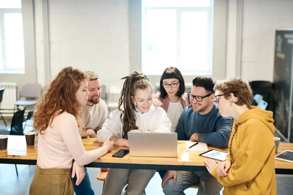 A diverse team of professionals collaborates happily around a laptop in a bright indoor setting. online course