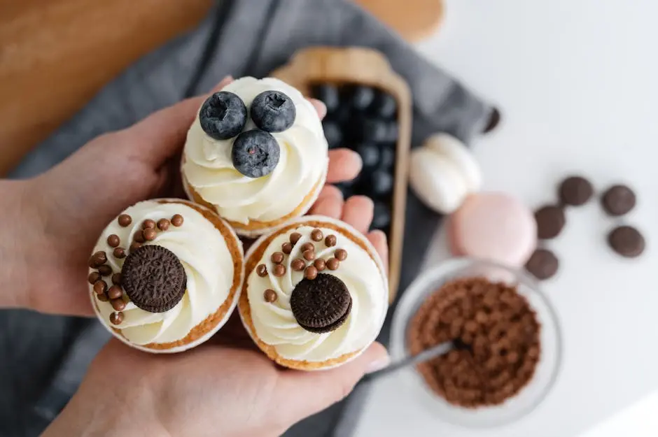 Top view of crop anonymous person showing delicious cupcakes with blueberries and chocolate sweets against blurred background of various dessert