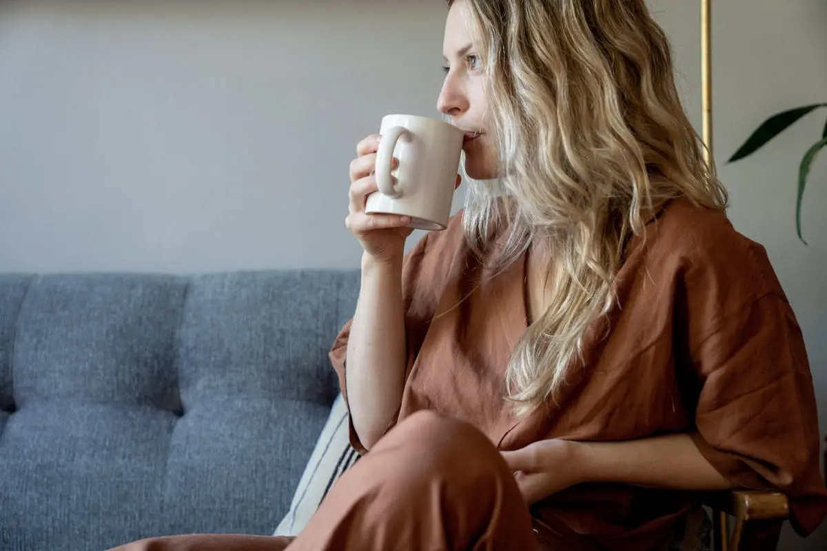 Woman with wavy blonde hair sipping coffee in casual indoor setting.