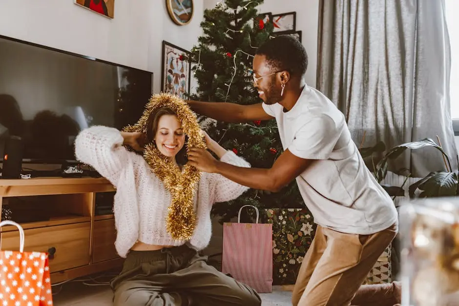 A couple playing with tinsel by the Christmas tree, sharing joyful moments indoors.