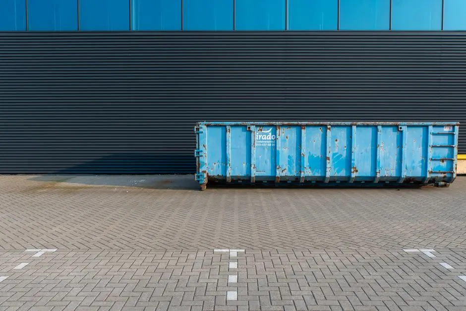A blue industrial dumpster placed beside a modern building facade, featuring clean lines and urban setting.