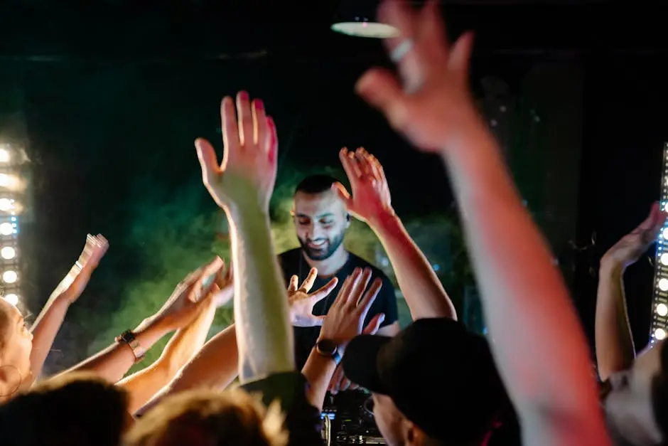 DJ performing live at a vibrant nightclub, people raising hands in excitement.