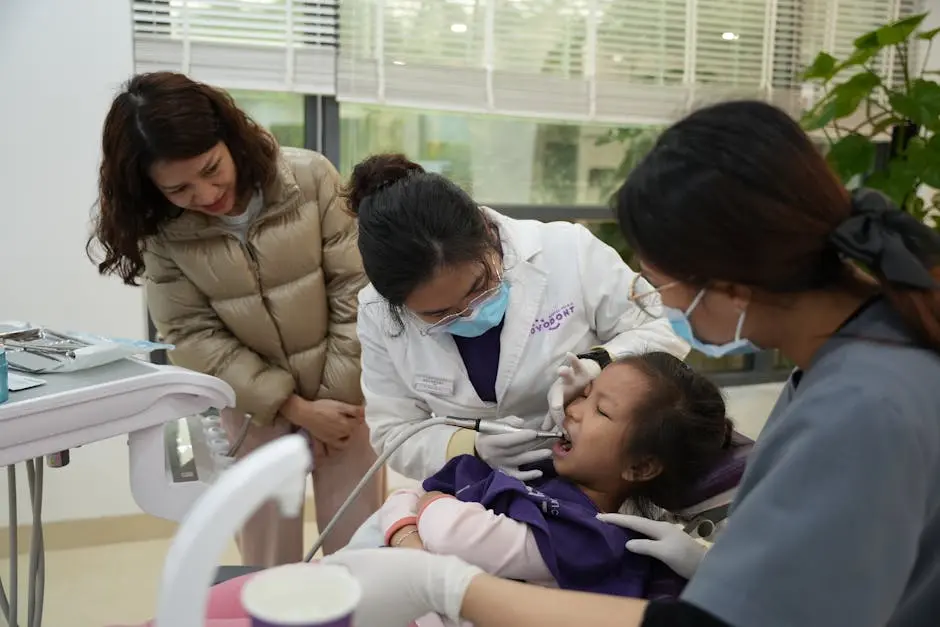 A dentist examines a young girl’s teeth, with a parent and assistant observing in a modern clinic.